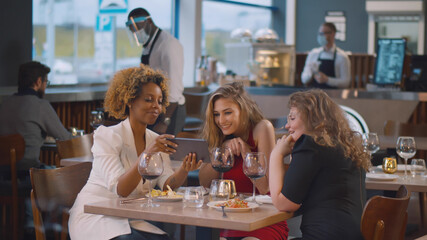 Diverse beautiful female friends in restaurant using tablet computer