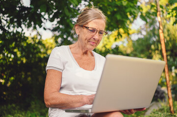 Happy senior old woman working online with laptop computer outdoor in garden