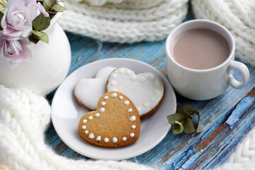 white knitted scarf, cup of coffee with milk and cookies in the form of hearts on a saucer