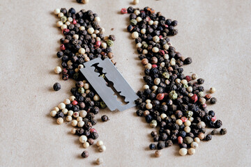 Macro shot image of Different color mixed dried peppercorns and razor blade on the beige pepper background. Concept of food ingredients and spices. Concept of stop drugs addiction. Narcotic anonymous