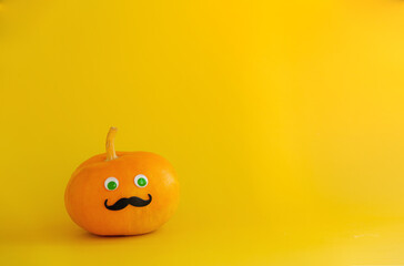Pumpkin in a witch hat with green eyes and mustache on Halloween on a yellow background