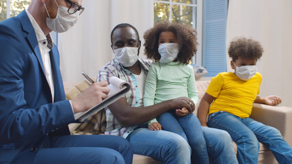 Insurance agent in mask consulting smiling young african man with kids at home.