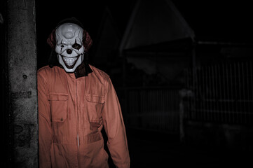 Asian handsome man wear clown mask with weapon at the night scene,Halloween festival concept,Horror scary photo of a killer in orange cloth