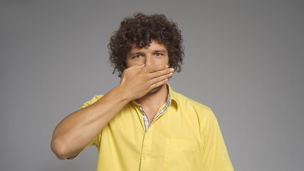 Fototapeta na wymiar Young Caucasian man covered his mouth with hand looking at camera. Isolated on gray background. Silence concept.