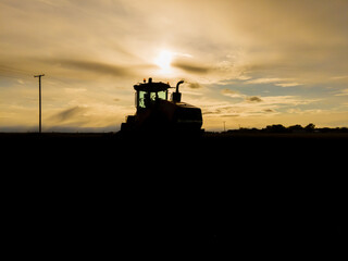 Fototapeta premium Tractor Silhouette in Field at Sunset in North Dakota.