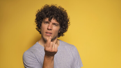 Fototapeta premium Romantic young man shows korean love sign. Shaggy guy folded two fingers together like mini heart looking into the camera. Cut out on white background.