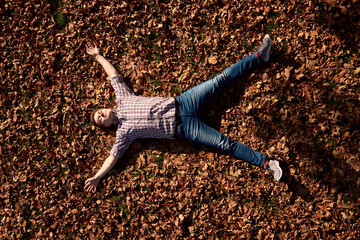 Happy young attractive man with closed eyes lying on the ground in autumn park and relaxing.