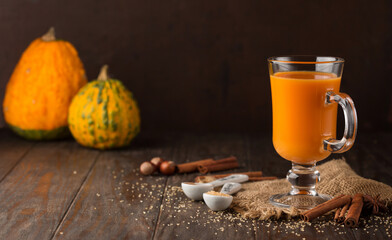 Pumpkin autumn hot drink with cinnamon and spices on old rustic wooden background.