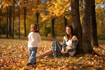 Fototapeta premium Happy woman and her daughter playing with leaves in autumn park