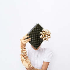 Woman in golden retro gloves hold gift box. Polka dots decor on white space background. Minimal fashion festive Christmas / New Year, holidays, birthday party, celebration concept.
