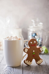 White mag of coffee with marshmallow and gingerbread snowman on a wooden table. Christmas break .