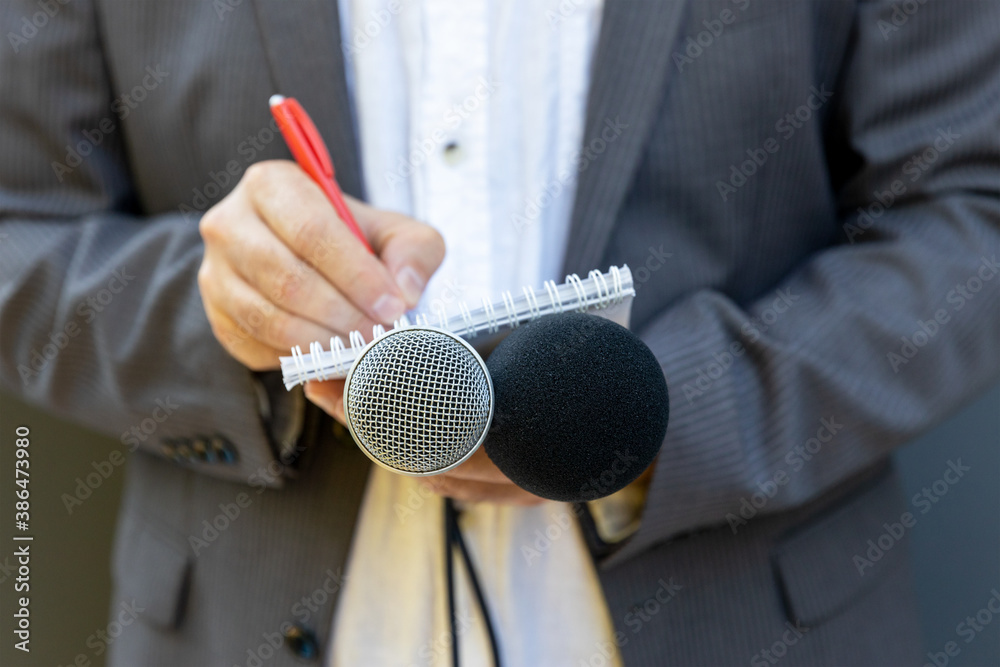 Wall mural Correspondent or reporter at media event, holding microphone, writing notes. Journalism concept.