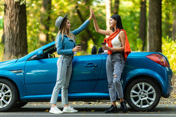 Beautiful young women giving high five, having fun together, cheering with raised arms driving...