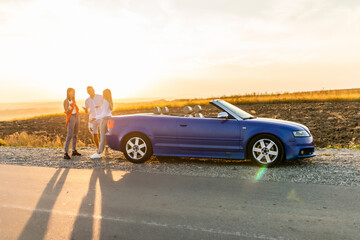 Young three friends standing near convertible car and talking each other have fun on beauty sunset on the road