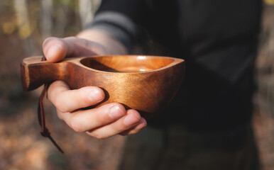 Fototapeta na wymiar A man holds a traditional wooden Kuksu mug. Autumn forest, close-up