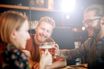 Couple standing in bar, toasting with beer and chatting with bartender.