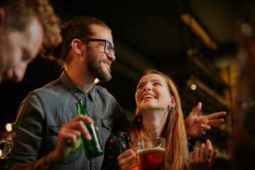 Lovely couple hanging on in bar with friends and drinking beer. Nightlife concept.