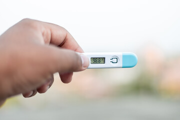 Sick man holds digital thermometer with body temperature reading in Fahrenheit up close to the camera.