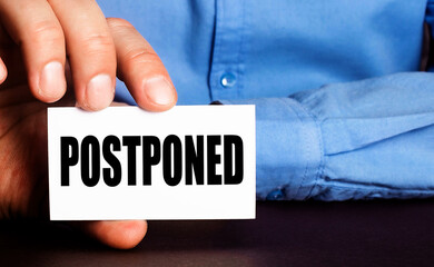 POSTPONED is written on a white business card in a man's hand. Advertising concept