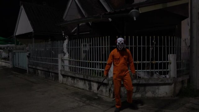 Asian handsome man wear clown mask with weapon at the night scene,Halloween festival concept,Horror scary photo of a killer in orange cloth	