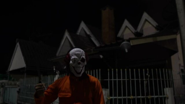 Asian handsome man wear clown mask with weapon at the night scene,Halloween festival concept,Horror scary photo of a killer in orange cloth	
