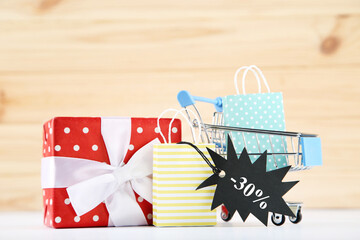 Gift box, shopping cart, black tag and paper bags on wooden background