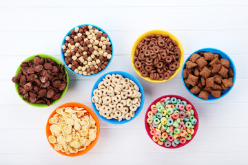 Various corn flakes in bowls on white wooden table