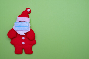 Santa Claus with protective mask on green background and copy space for text. Cute santa claus made of cloth.