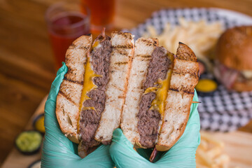 PRIMER PLANO DE HAMBURGUESA DE QUESO CON TOCINETA EN MANOS DE UNA PERSONA
