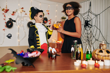 Excited kids in Halloween costumes drinking sweet cocktails decorated with paper pumpkins