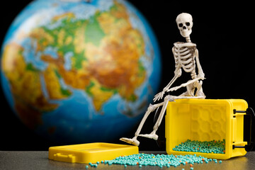 a skeleton on a box from which small green beads fell, behind a blurry globe
