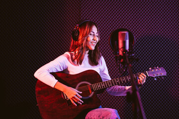 Pretty Asian female singer recording songs by using a studio microphone and pop shield on mic while...