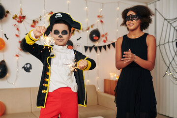 Teenage girl clapping to younger brother in pirate costume burning Bengal lights at Halloween party