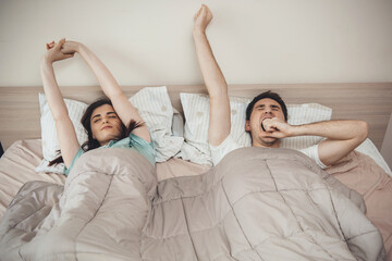 Caucasian couple yawning in bed and stretching in the morning covered with a quilt