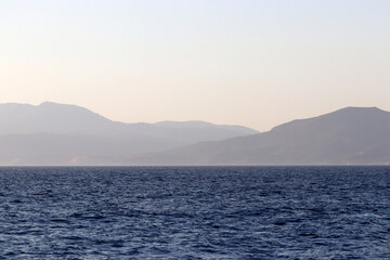 View from the sea to the mountainous islands, coast in the morning. Picturesque seascape, coastline with hills covered by forest in a mist