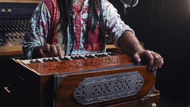 Music production studio. Creative world. Hindi man playing harmonium in the sound studio. A long hair brunette male person in a traditional shirt plays meditation music.