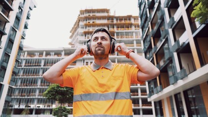 Builder covers his ears, ear muff to protect workers ears. Construction worker wearing protective ear defenders. Concept of construction, taking care of safety during work. Protection against injury