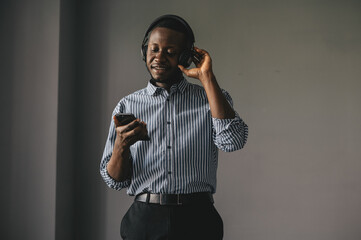 Young african man listening to music with wireless earphones and dancing at home