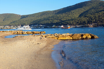 Fototapeta premium Sandy coast, mountains, boat and azure Aegean sea on a bright sunny day. Travel to Turkey. Beautiful seascape.