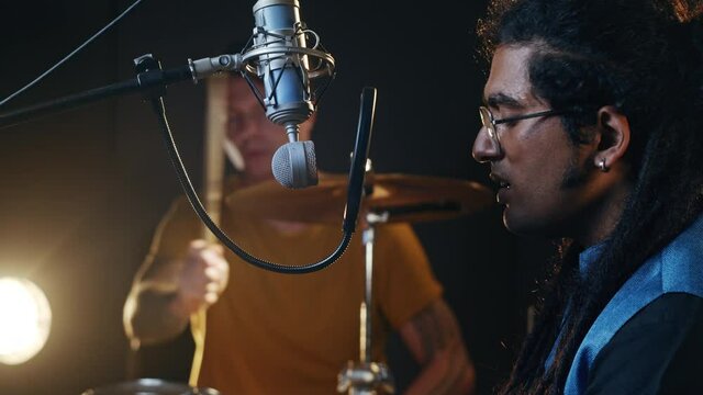 Music production studio. Band rehearsal. Caucasian man playing drums, indian man singing. Talented musicians record their ideas.