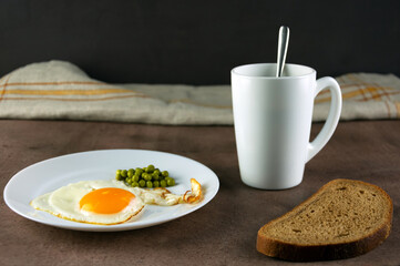 Traditional breakfast, fried eggs, bread, coffee in a white cup on a dark background. Horizontal orientation