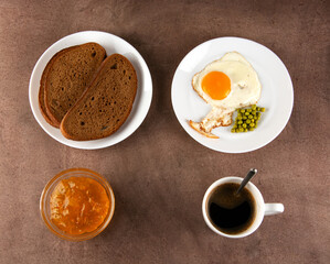 Classic breakfast: fried eggs, jam, bread, coffee in a white cup on a brown background. Top view