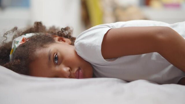 Little cute african american girl lying on bed and smiling at camera