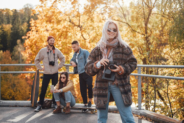 Obraz premium Pretty girl with blond hairs and camera posing in foreground in autumn landscape background and her friends in daytime.