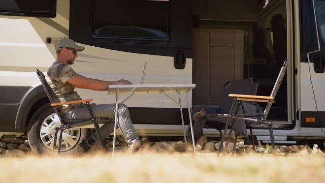 Summer Camper Van Road Trip and Remote Computer Work. Men Working on His Laptop Outside of His RV.