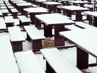 Fototapeta na wymiar Wooden identical tables with benches covered with snow are placed in a row. Street Cafe