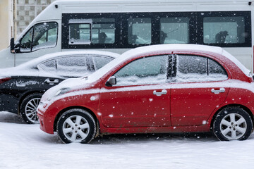 Snowfall. Cars dusted with snow are parked near the building.