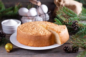 Homemade round sponge cake or chiffon cake on white plate so soft and delicious with ingredients: eggs, flour, milk on wood table. Basis for making holiday cakes and desserts. 
