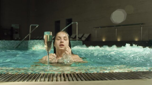 Pretty girl emerging water at spa pool. Young woman sipping champagne in spa