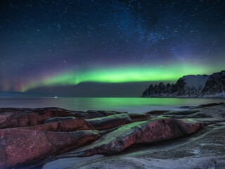 Fototapeta na wymiar Tungeneset rocks and Aurora Borealis light. Stars trails and northern light. Reflections on the water surface. Senja islands, Norway. Travel - image